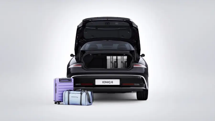 Vista traseira do IONIQ 6 com bagageira aberta e malas pousadas ao lado no chão