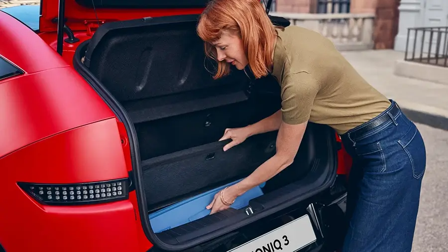 Mulher a guardar itens na bagageira do Hyundai IONIQ 3 vermelho