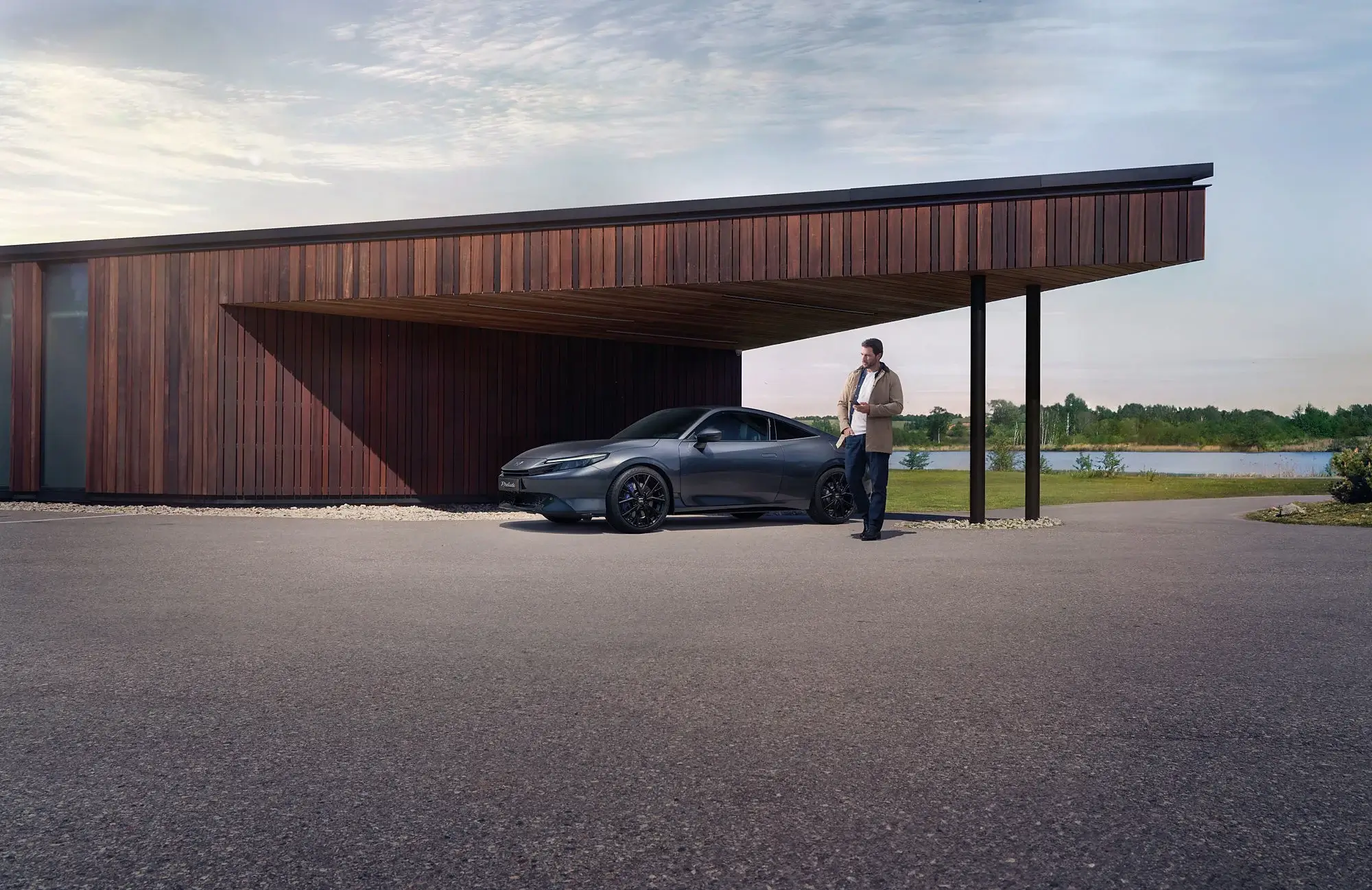 Homem ao lado de Honda Prelude com casa de madeira escura atrás