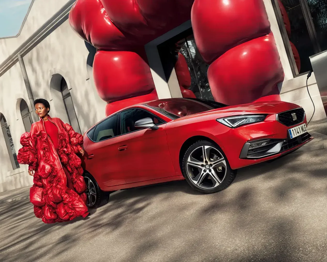 Mulher vestida de vermelho ao lado de SEAT Leon vermelho